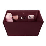 A burgundy fabric organizer pouch shown from above, filled with travel accessories including a pink water bottle, a phone case, a small card holder, and a white item.
#color_mulberry