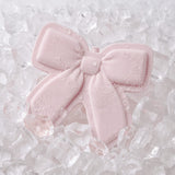 A pale pink bow-shaped ice pack with water droplets, resting on a bed of clear ice cubes.