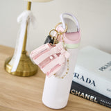 Pink shoe keychain with decorative elements on a white stand, with Prada and Chanel books in the background.
#color_ballet pink bow