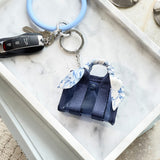 Keychain with a small bag charm on a marble surface
#color_something navy twilly