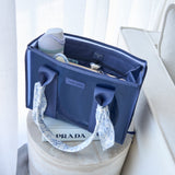 A navy blue bag with patterned fabric handles sits on a round pedestal, with a water bottle and other items inside, in a softly lit indoor setting.
#color_oxford navy