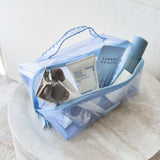 A light blue translucent zippered cosmetic bag filled with skincare and beauty items, placed on a round stone surface against a soft neutral background.
#color_carolina blue crochet wave