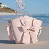 Ice cubes falling into a pink cooler with a large bow on a sandy beach with ocean and clear sky in the background
#color_ballet pink bow