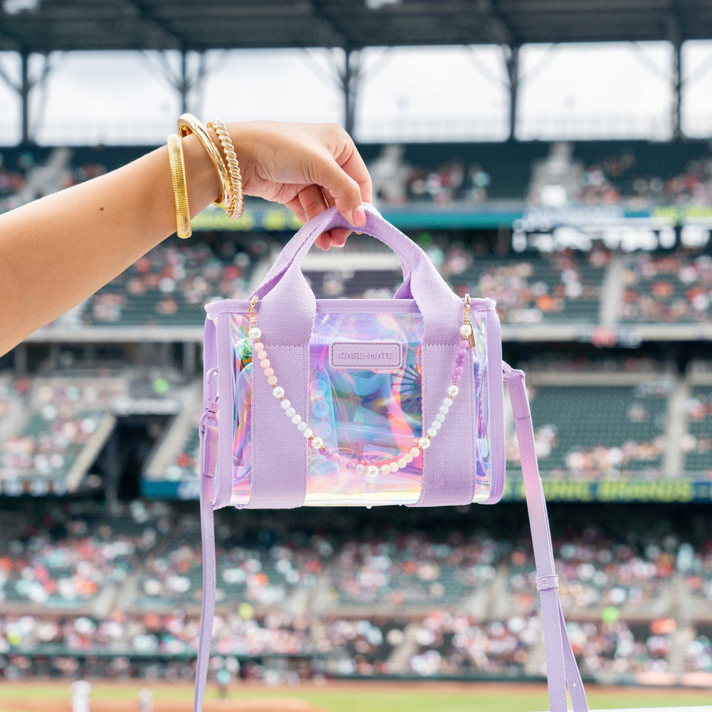 Person holding a transparent purple handbag with a colorful chain in front of a stadium. #color_iridescent