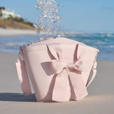 Ice cubes falling into a pink cooler with a large bow on a sandy beach with ocean and clear sky in the background
#color_ballet pink bow