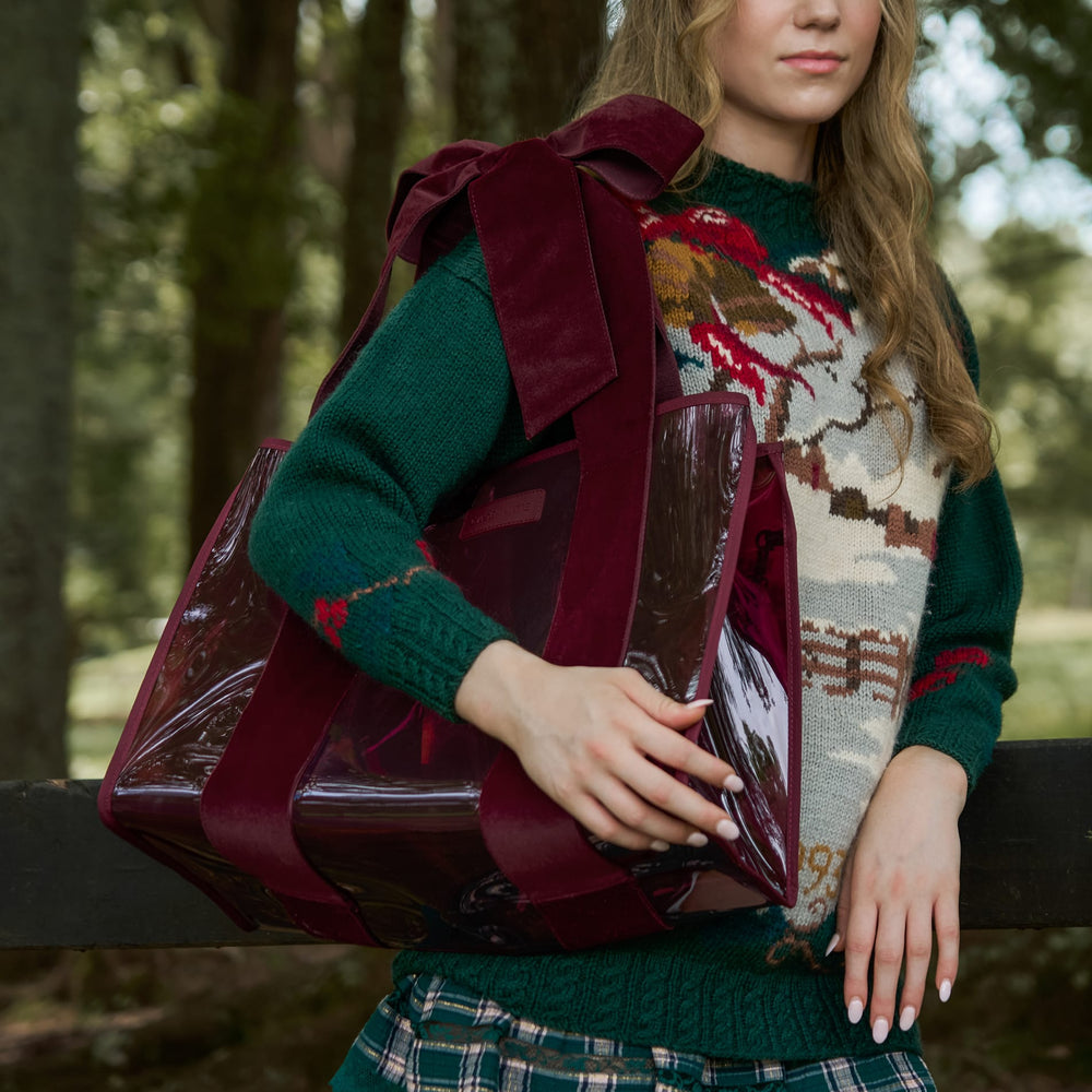 Woman in a holiday sweater outdoors ina. woodsy setting with a red velvet bow jelly tote bag. #color_holiday edition red velvet bow