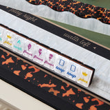 A close-up of a deck of playing cards arranged in a row on a white plastic card holder, with a black and orange leopard-print deck border and a matching black card deck mat underneath. The cards feature white backs with printed names and symbols including 'joker', 'north', 'flower', 'soap', and 'joker' in colorful fonts.
#color_tortoiseshell pearl edition