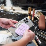 Person holding a phone case with a purple textured design on a marble surface with makeup items.
#color_stardust