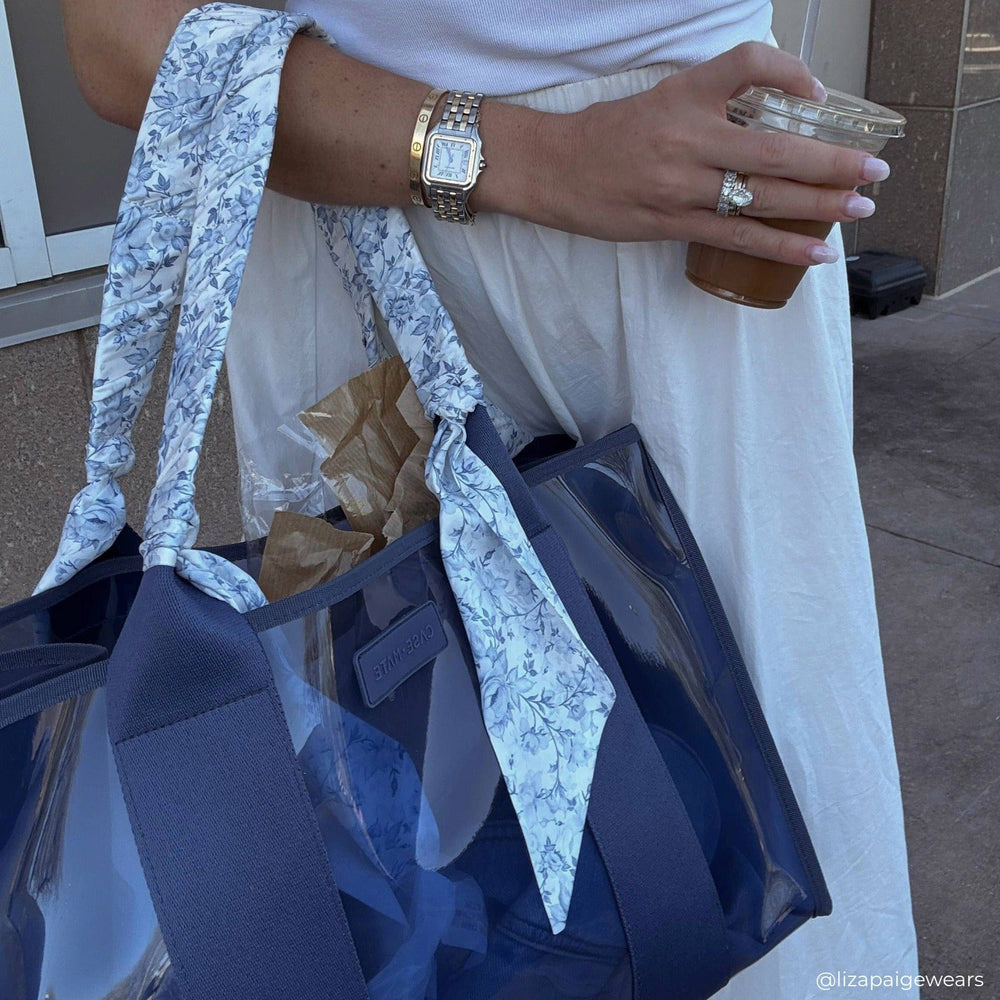 Person holding a blue bag with a floral scarf, wearing a watch and ring, outdoors.
#color_something navy twilly