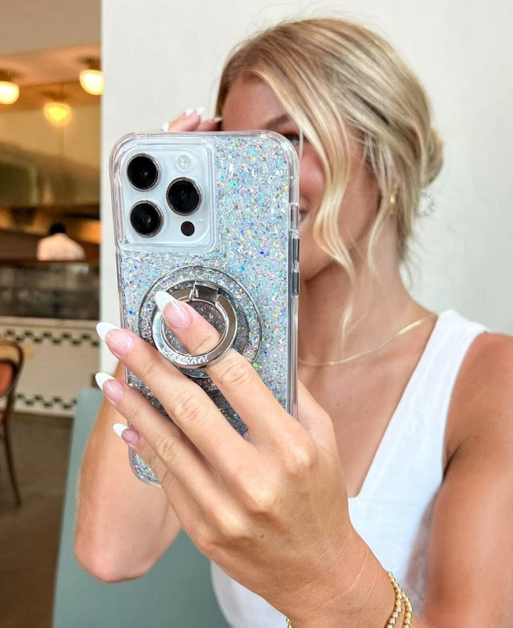 Person holding a phone with a glittery case and ring holder in a kitchen setting