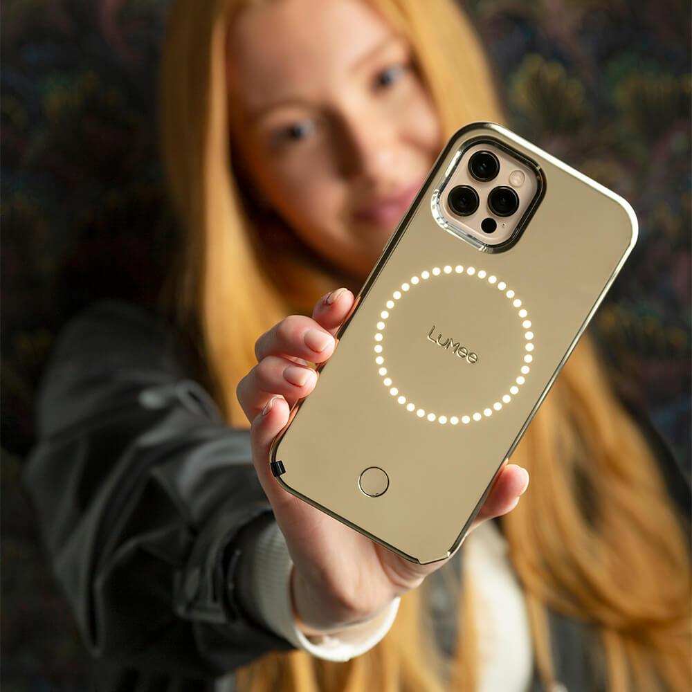 Woman holding gold mirror light up LuMee case out in front of her. color::Gold