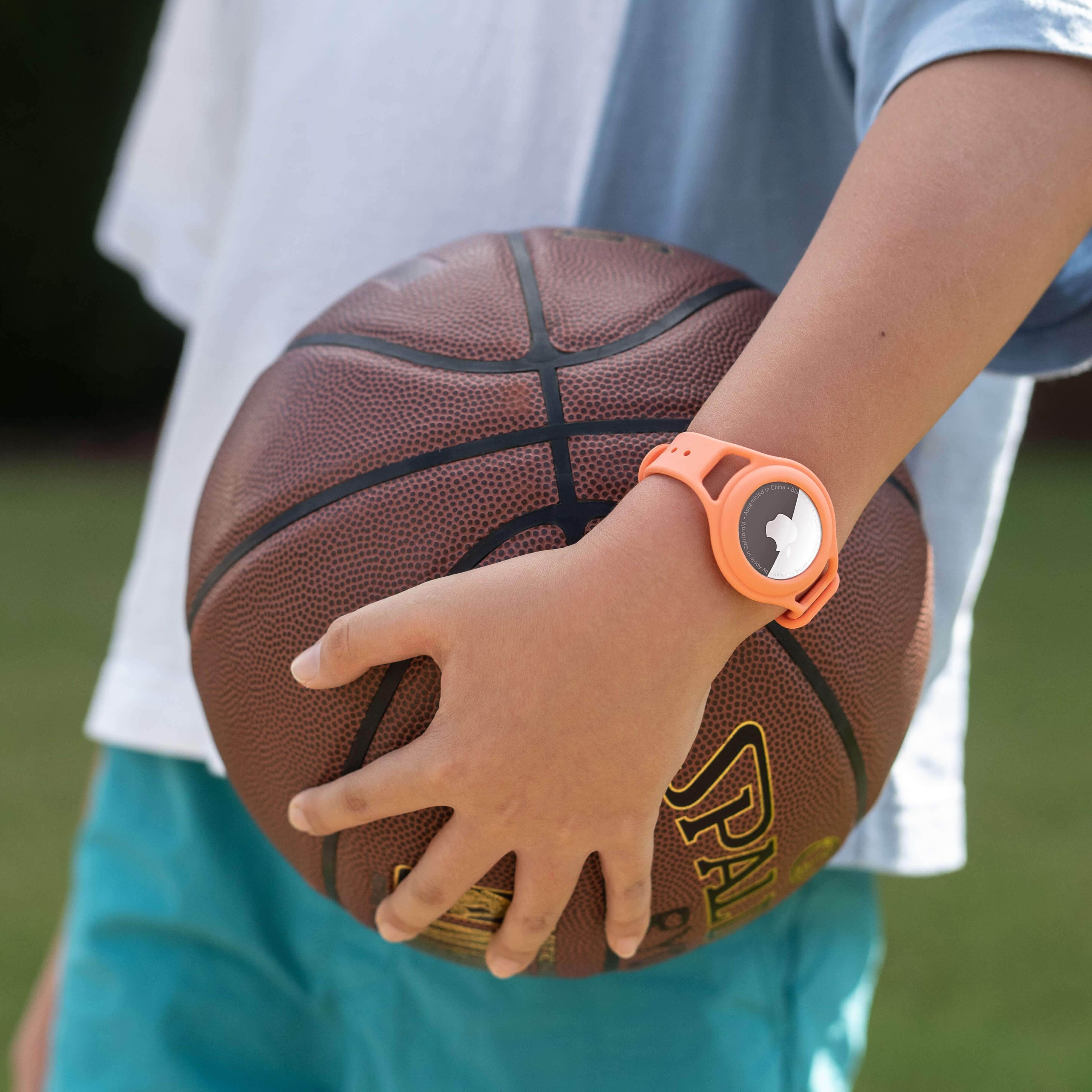 Child wearing tracker strap bracelet while holding basketball. color::Coral