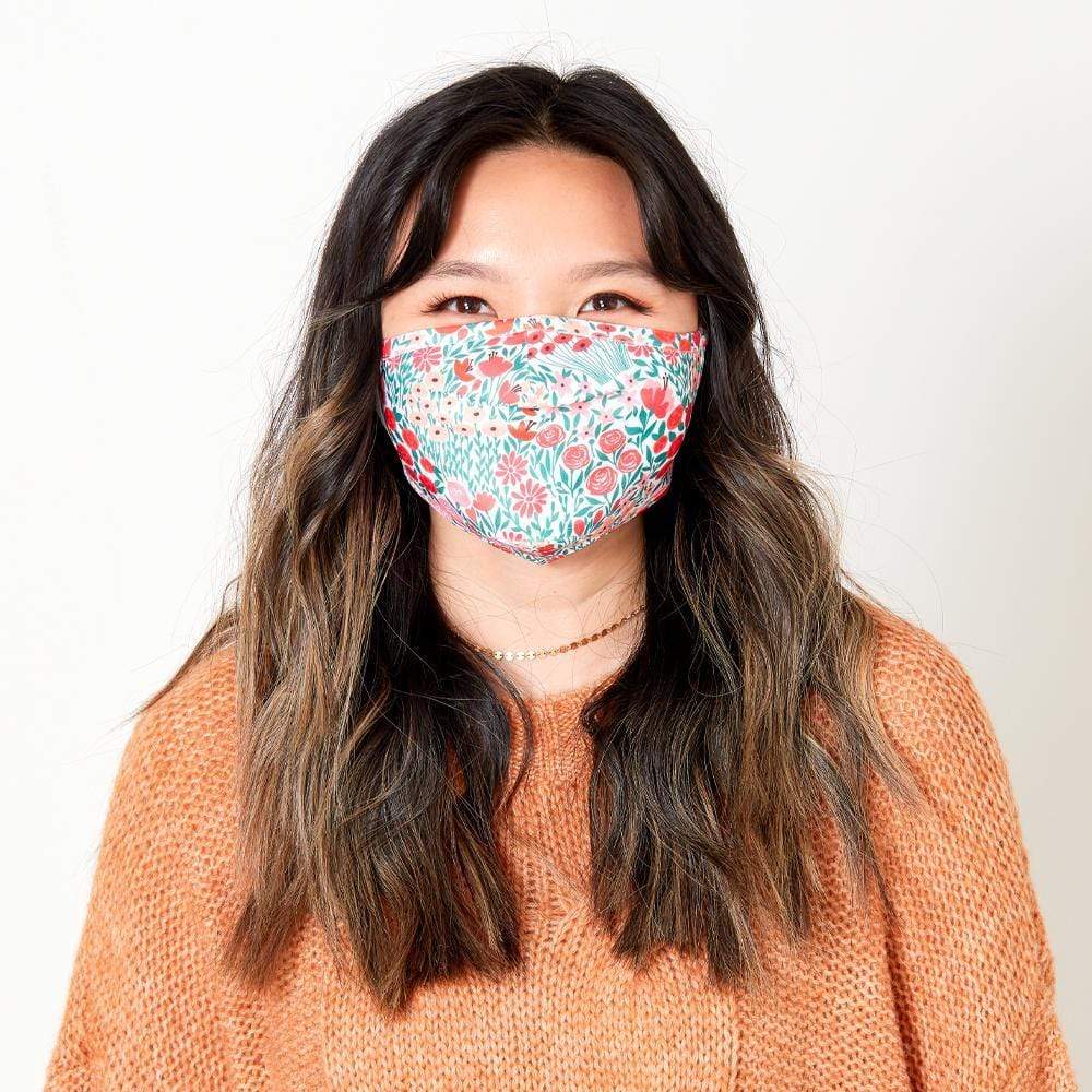 Woman wearing bright floral cloth face mask. color::Warm Meadow