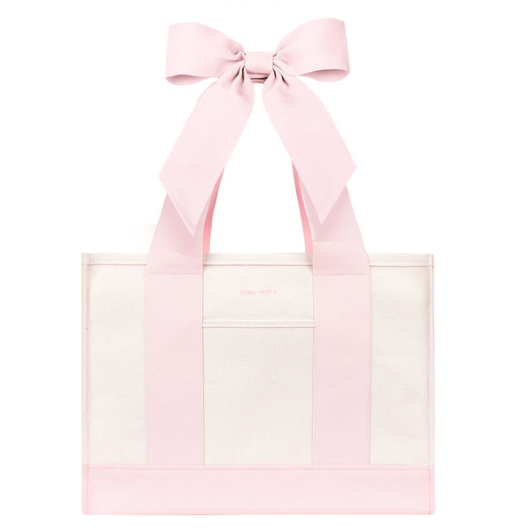 A light pink and white tote bag with wide pink shoulder straps and a large matching pink bow at the top, shown on a plain white background.
#color_ballet pink bow