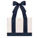 An off-white canvas tote bag with bold navy blue vertical stripes and matching navy ribbon handles tied in a large bow at the top. The brand name 'CASE-MATE' is printed in small black letters on the front pocket.
#color_oxford navy bow