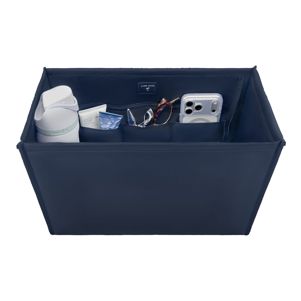 A navy blue fabric organizer tray with multiple interior pockets, shown holding a white bottle, a small blue item, eyeglasses, and a silver smartphone. The organizer is photographed on a clean white background.

#color_navy