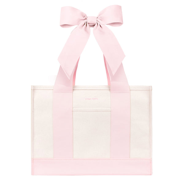 A light pink and white tote bag with wide pink shoulder straps and a large matching pink bow at the top, shown on a plain white background.
#color_ballet pink bow