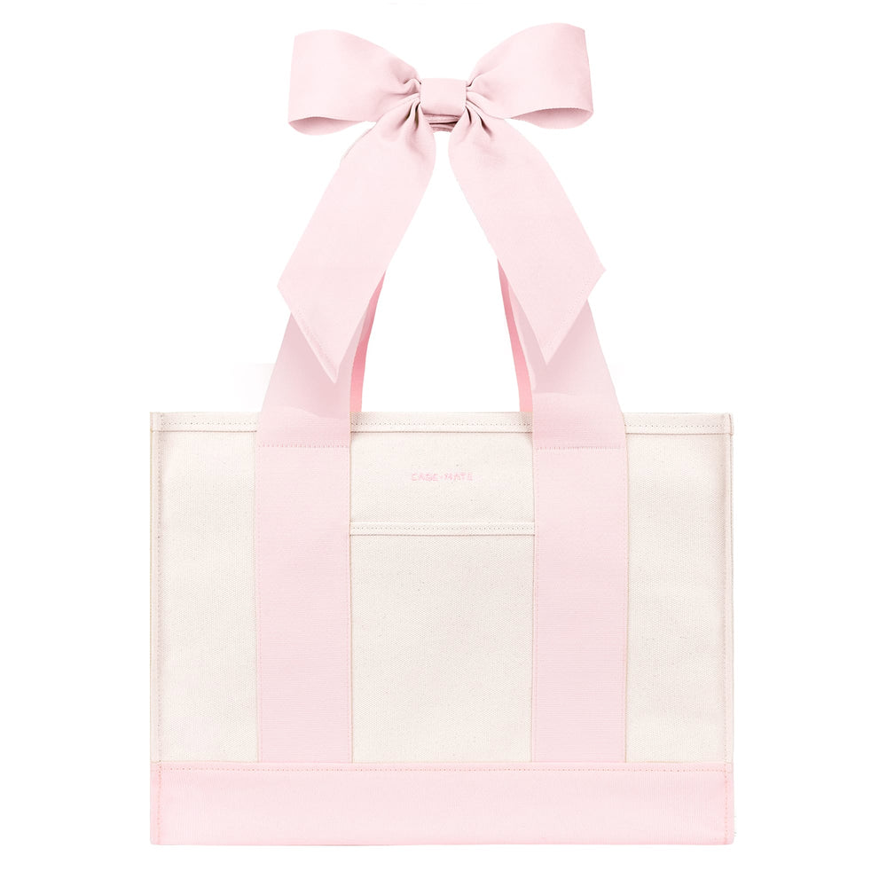 A light pink and white tote bag with wide pink shoulder straps and a large matching pink bow at the top, shown on a plain white background.
#color_ballet pink bow