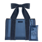 A dark blue denim strap jelly tote bag with matching denim shoulder straps and a large bow, shown alongside a matching translucent phone pouch on a plain white background.
#color_dark wash denim bow