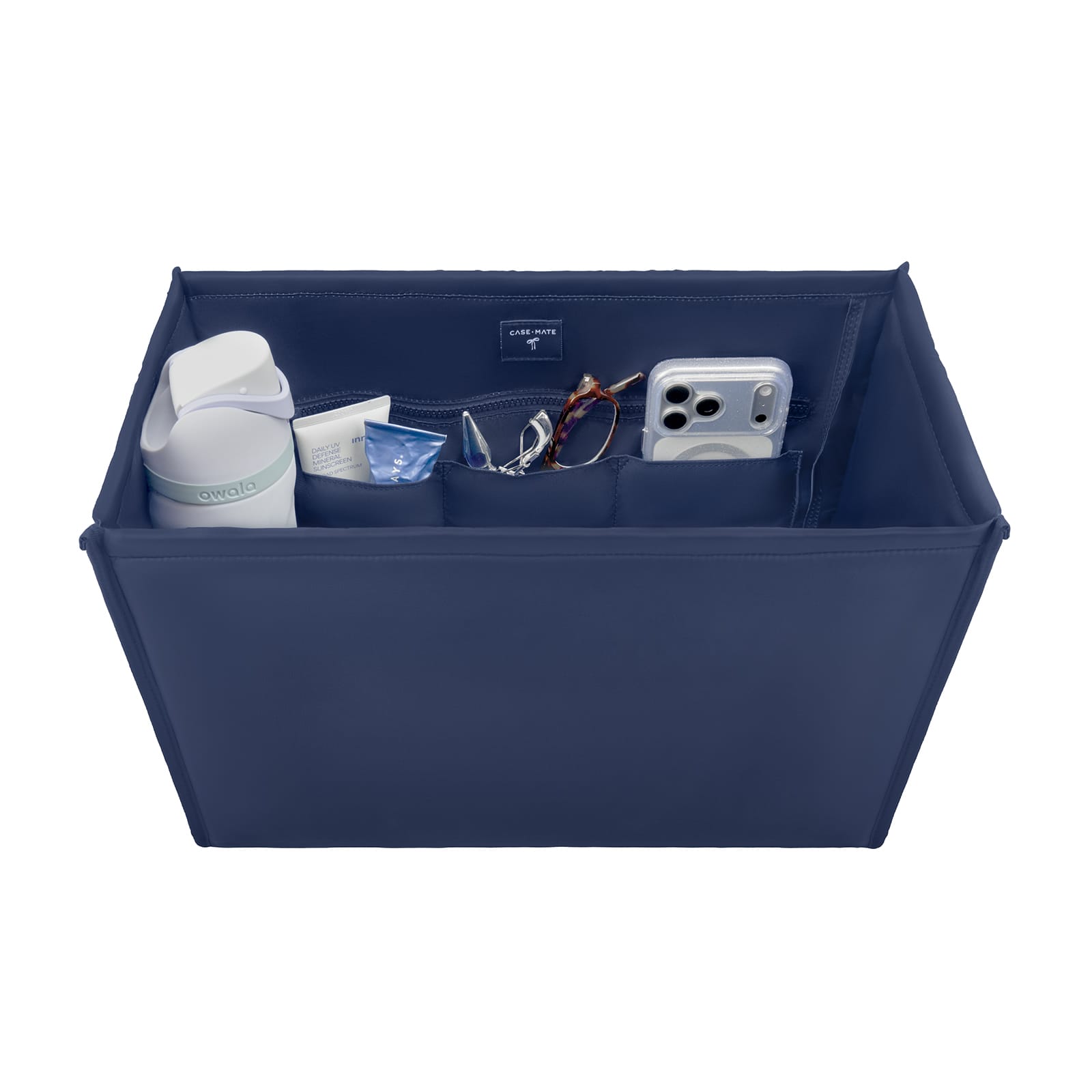 A navy blue fabric organizer box with multiple interior pockets, shown holding various items including a white bottle, a small tube, a pair of sunglasses, and a silver smartphone. The box is photographed on a clean white background.

#color_oxford navy