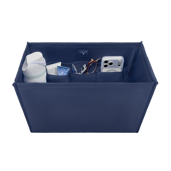 A navy blue fabric organizer box with multiple interior pockets, shown holding various items including a white bottle, a small tube, a pair of sunglasses, and a silver smartphone. The box is photographed on a clean white background.

#color_oxford navy