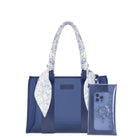 A navy blue tote bag with a white and blue floral patterned scarf tied to its handles, shown next to a matching translucent navy blue phone pouch on a solid white background. 
#color_something navy twilly 