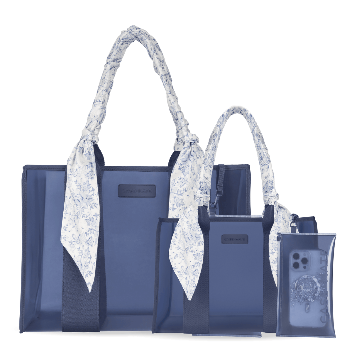 A coordinated set of navy tote bags and matching accessories on a white background, including two tote bags with long white handles patterned with small blue flowers, a matching zip pouch, and a clear phone case with a blue floral insert.