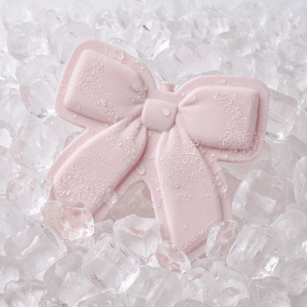 A pale pink bow-shaped ice pack with water droplets, resting on a bed of clear ice cubes.