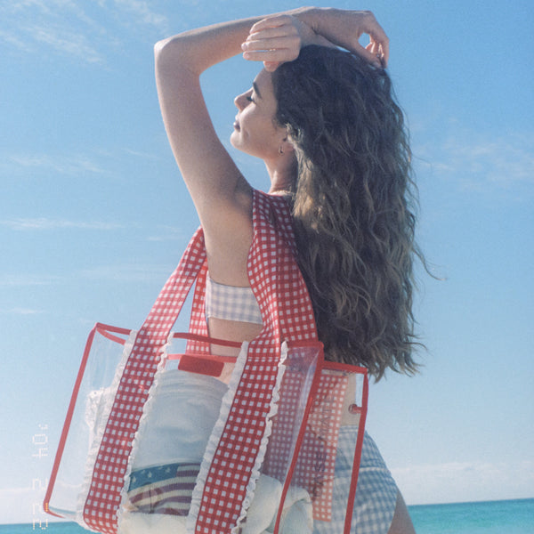Woman on a beach with a red and white checkered cover-up and red gingham bag 
#color_Cherry Gingham