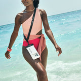 Woman in a pink and red swimsuit standing on a beach with clear blue 
water. #color_sand dollar