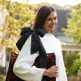 Woman holding a tortoiseshell patterned bag with a large black bow outdoors #color_tortoiseshell bow