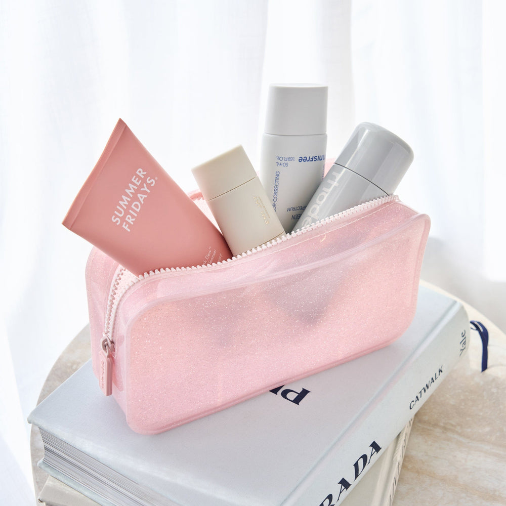Pink cosmetic bag with skincare products on top of a book