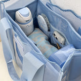 A light blue fabric organizer tote bag shown open, filled with toiletries and accessories including a bottle, phone, brush, and small items. The bag has multiple compartments, zipper pockets, and a soft structured shape.

#color_carolina blue