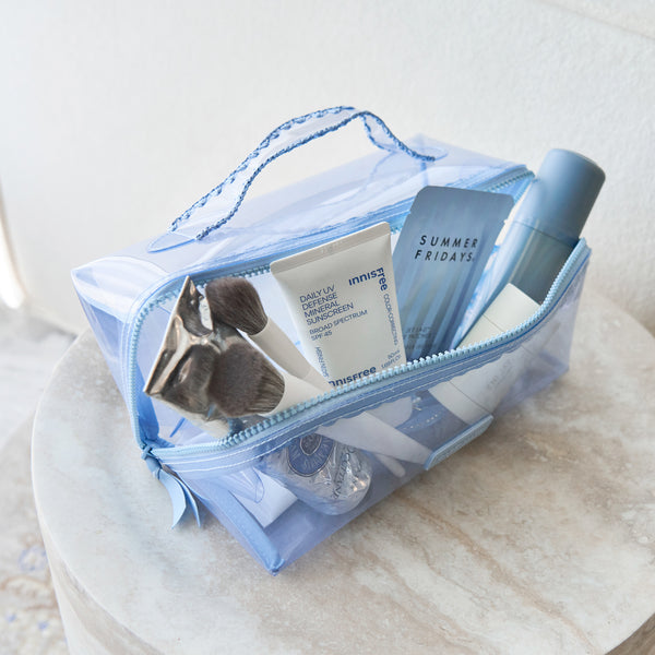 A light blue translucent zippered cosmetic bag filled with skincare and beauty items, placed on a round stone surface against a soft neutral background.
#color_carolina blue crochet wave