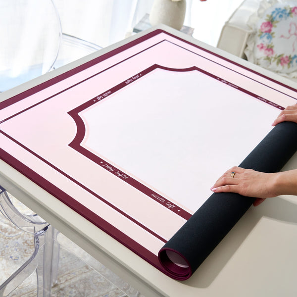 A person's hands are shown unrolling a black mat over a pink and white printed template sheet on a light-colored table. The mat has a dark burgundy border with white text.
#color_classic ballet pink
