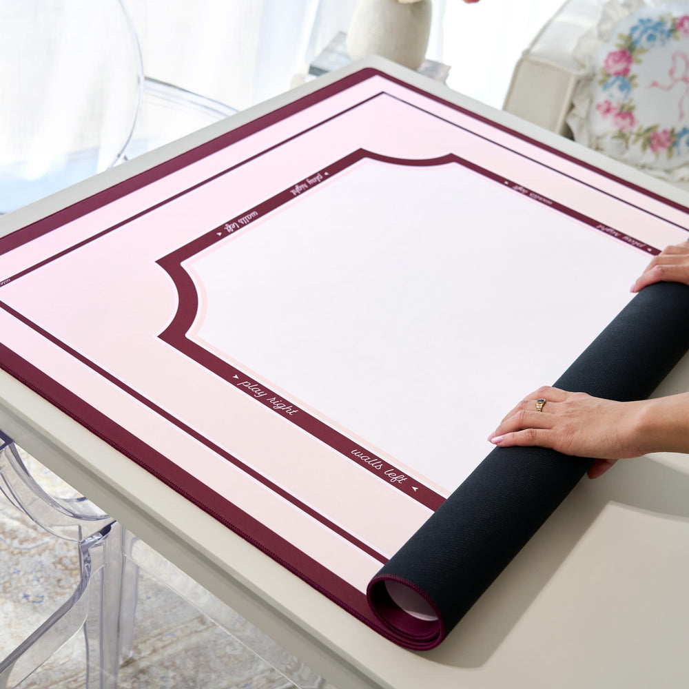 A person's hands are shown unrolling a black mat over a pink and white printed template sheet on a light-colored table. The mat has a dark burgundy border with white text.
#color_classic ballet pink