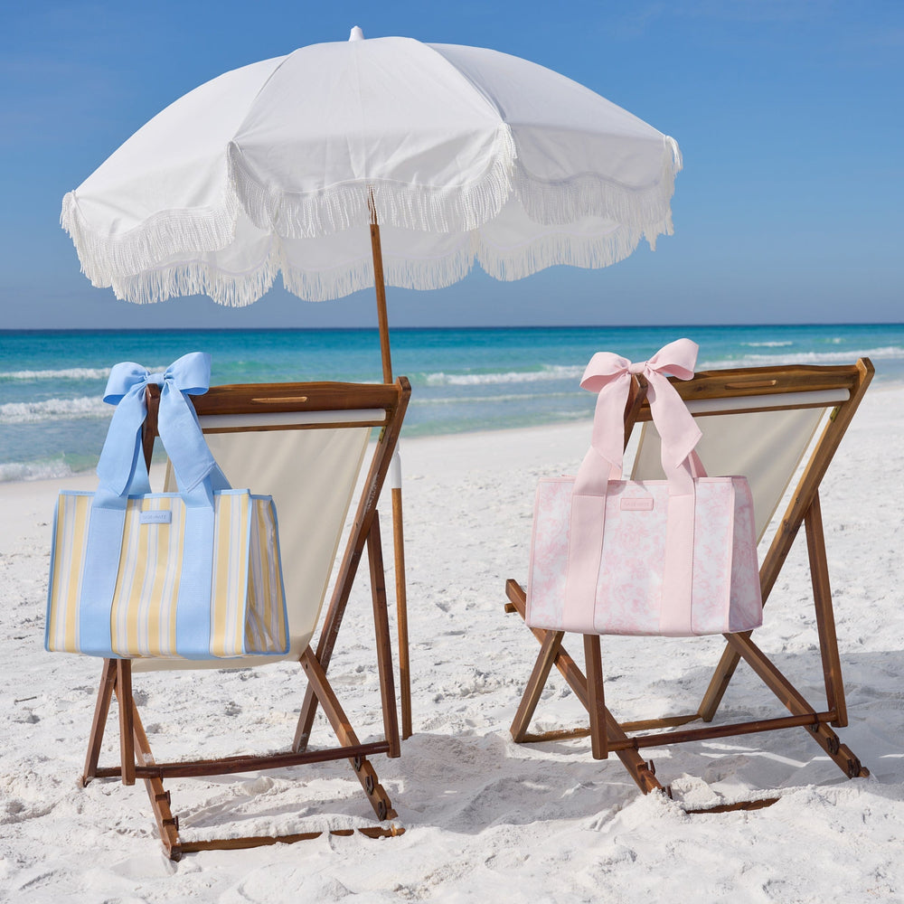 Two beach chairs with striped bags and a white umbrella on a sandy beach.