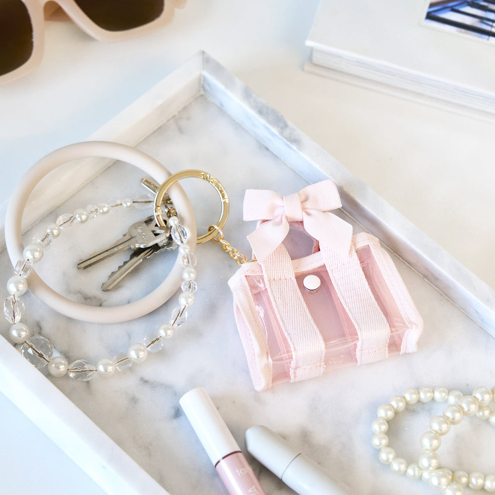 Pink keychain with a bow, pearl bracelet, and keys on a marble surface. #color_ballet pink bow