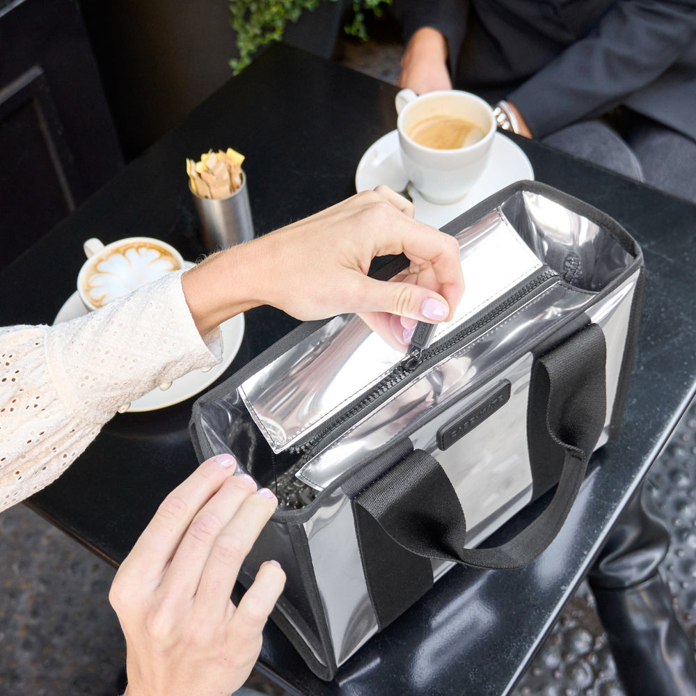 Person using a clear bag with black handles at a cafe table with coffee and pastries.
#color_silver chrome