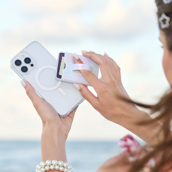 Person using a phone case applicator on a smartphone with a blurred beach background
#color_iridescent