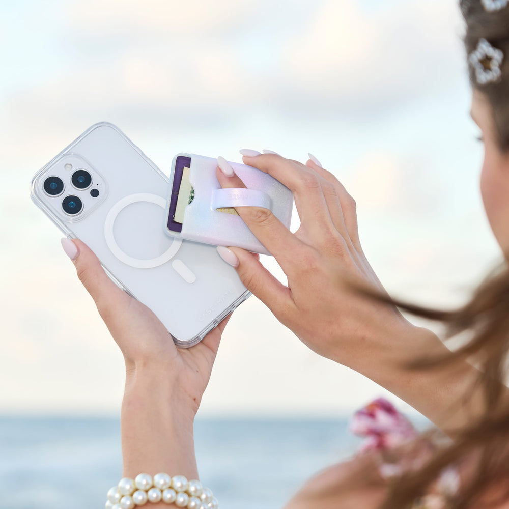 Person using a phone case applicator on a smartphone with a blurred beach background
#color_iridescent