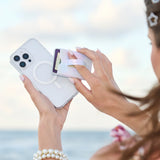 Person using a phone case applicator on a smartphone with a blurred beach background
#color_iridescent