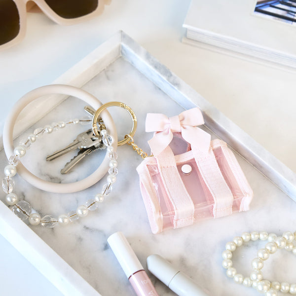 Pink keychain with a bow, pearl bracelet, and keys on a marble surface.
#color_ballet pink bow