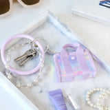 Keychain with pink bag charm, keys, and bracelet on a marble surface with a bottle and book.
#color_iridescent