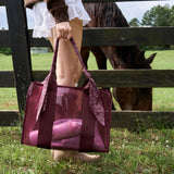 A person standing in a grassy field beside a wooden fence holds a sheer burgundy tote bag with a matching fabric bandana-style handle. A horse is visible behind the fence in the background.
#color_mulberry twilly