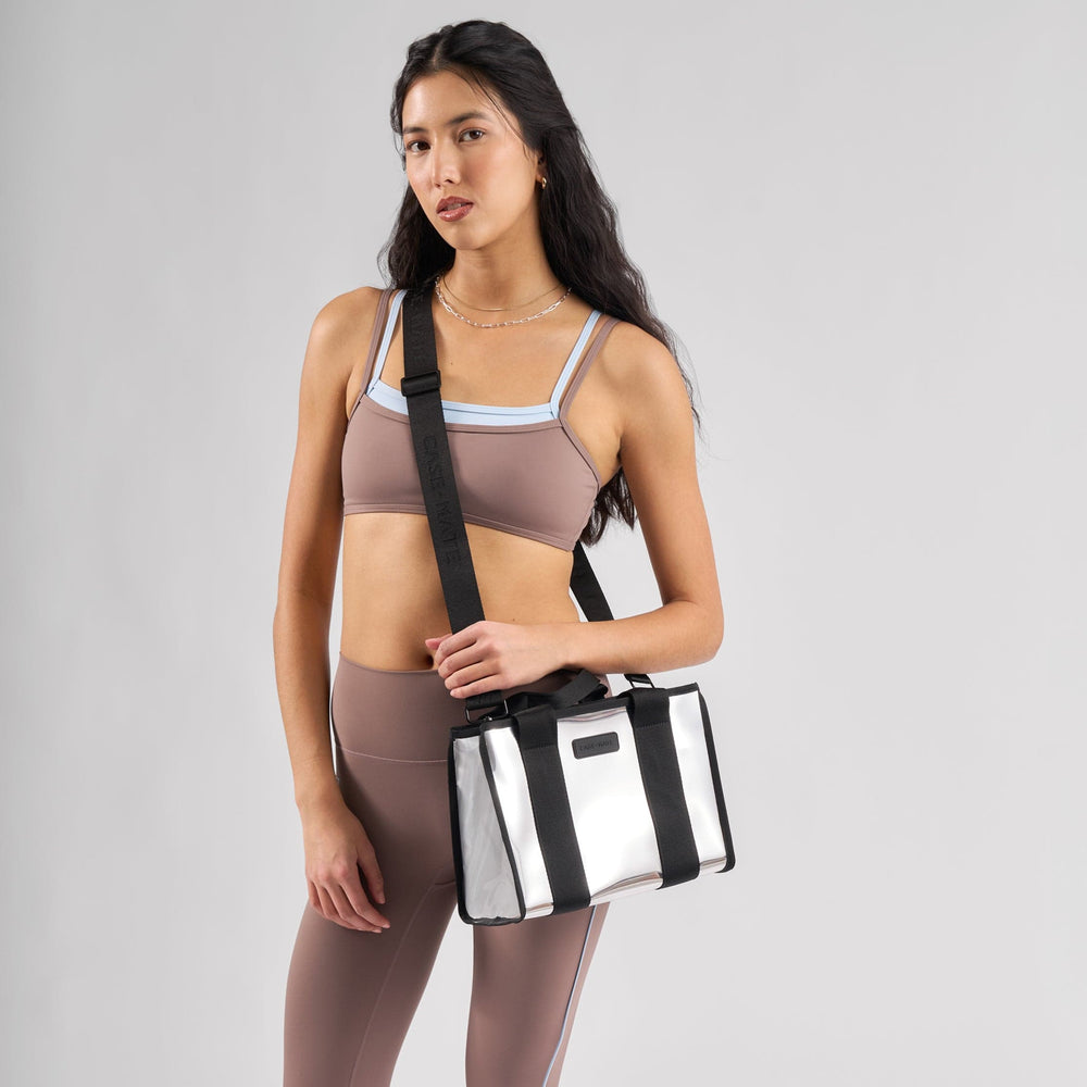 Woman in athletic wear holding a black and silver bag against a gray background