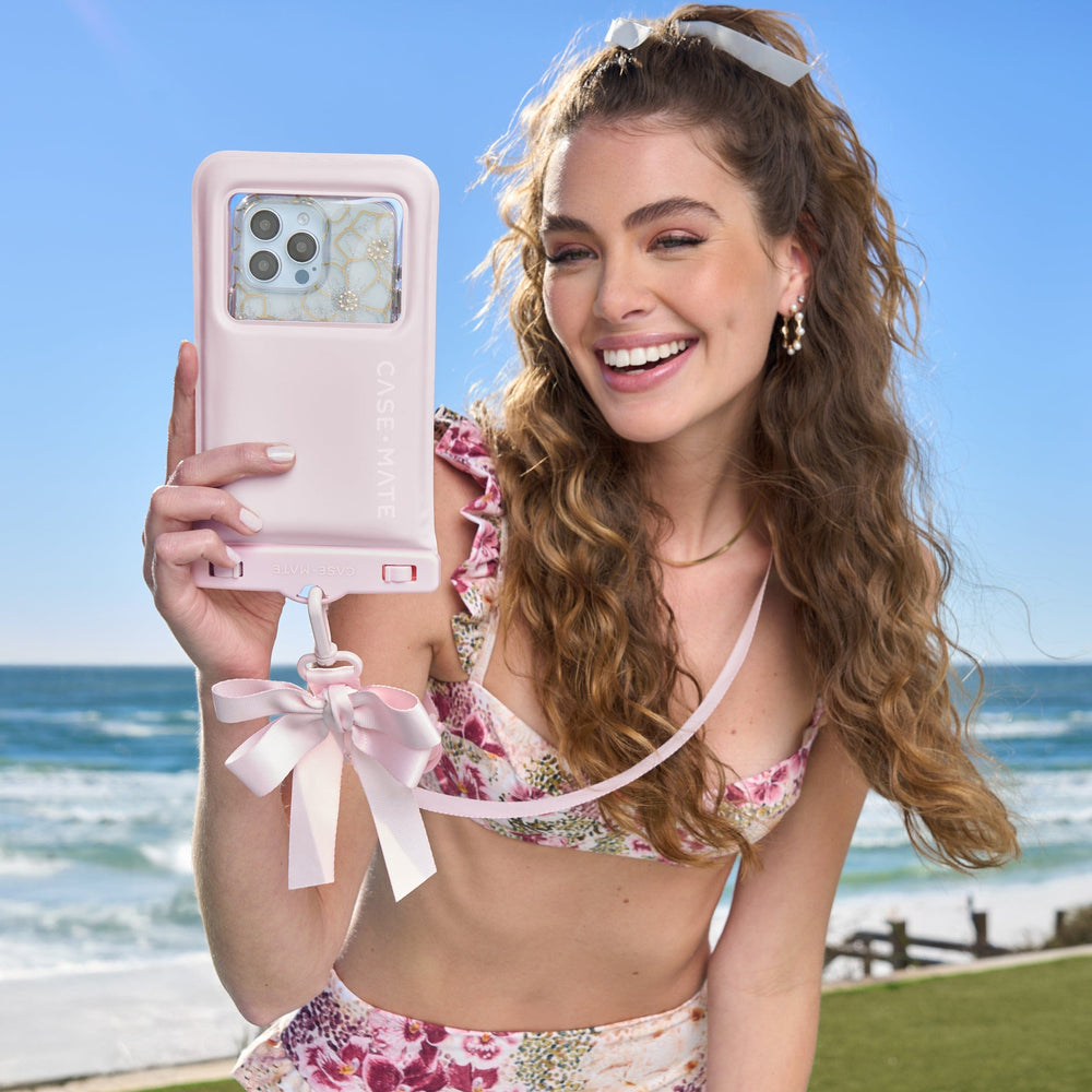 Woman holding a pink phone case with a scenic ocean background