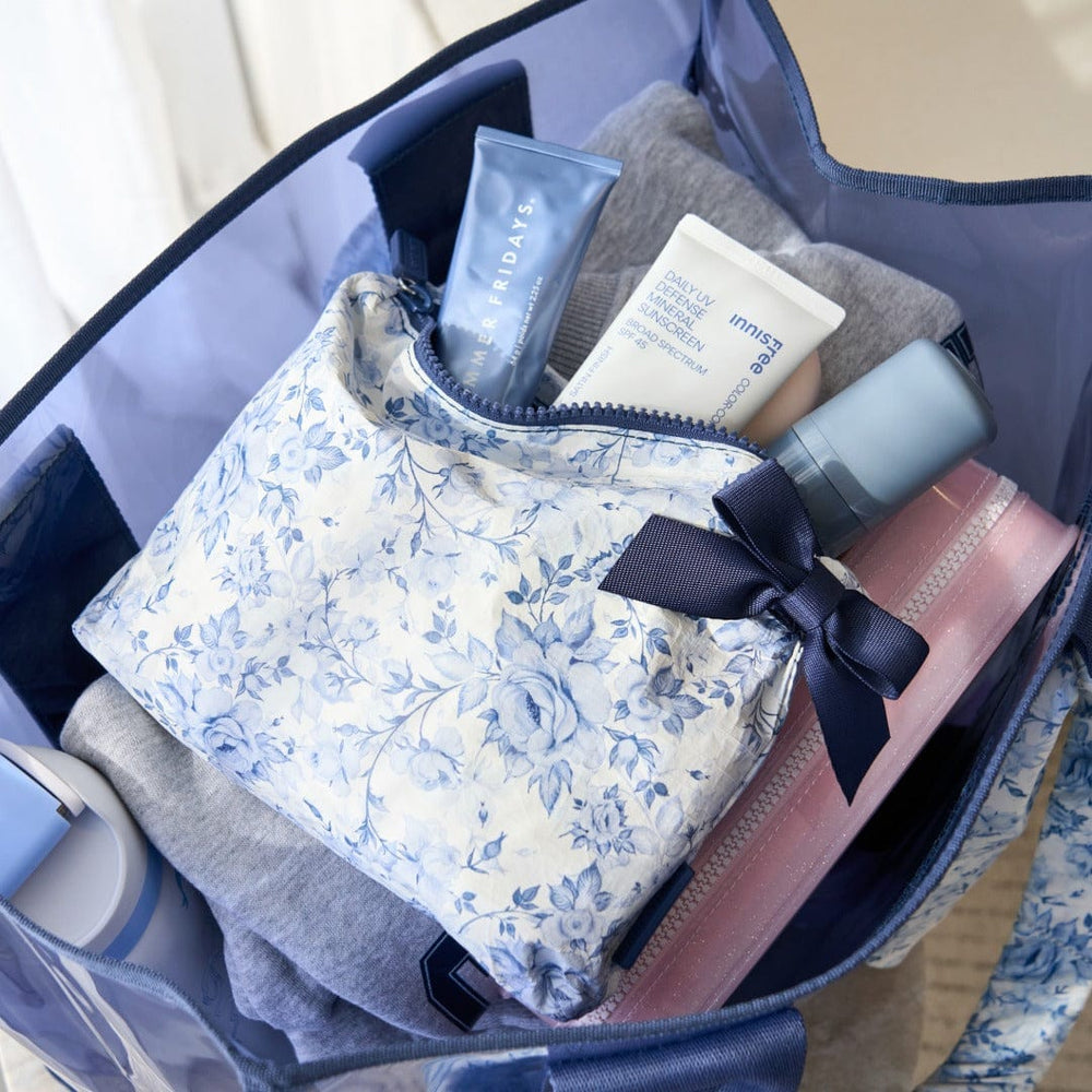Open suitcase with travel essentials including a floral pouch, bottles, and a hairbrush.
#color_something navy bow