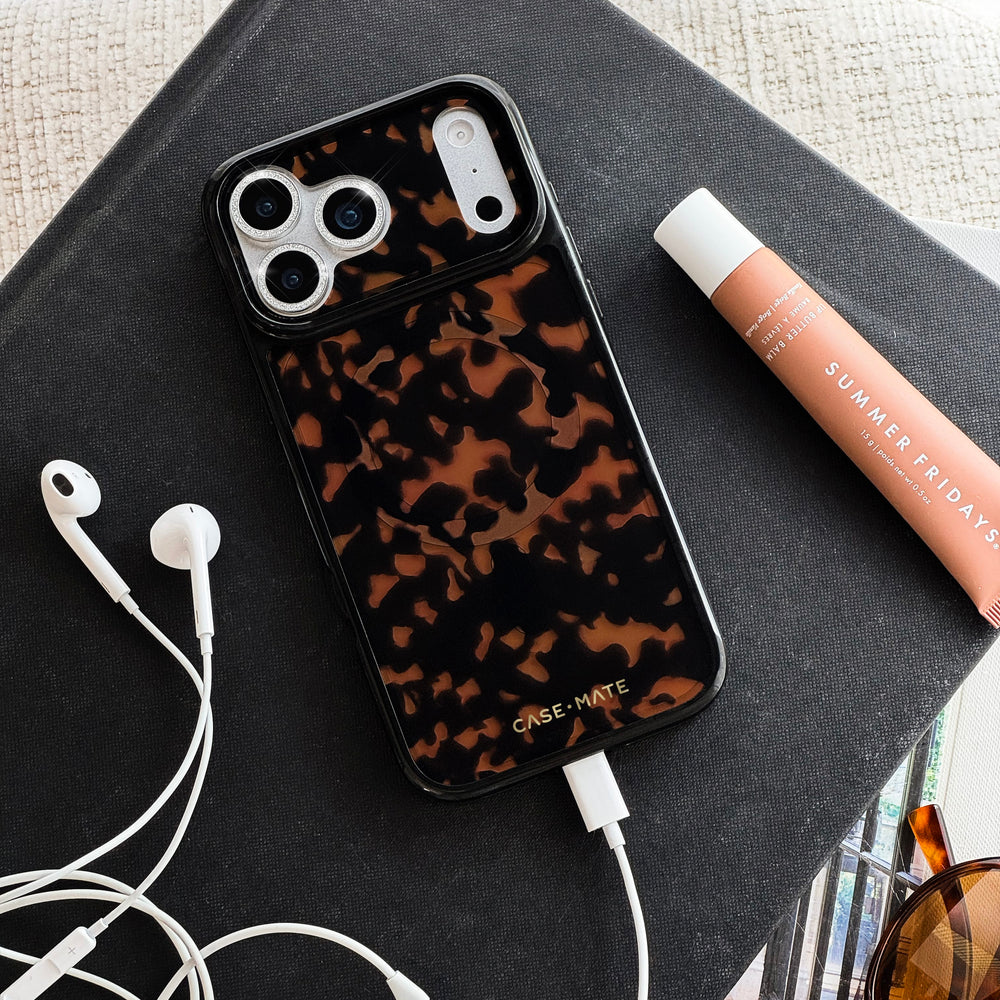 Tortoiseshell patterned iPhone case with white charging port and camera cutouts on dark fabric surface.