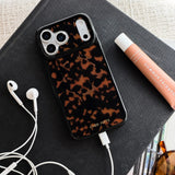 Tortoiseshell patterned iPhone case with white charging port and camera cutouts on dark fabric surface.